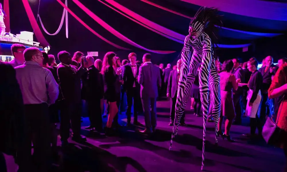 Black-and-white striped stilt performer entertaining a crowd inside a colorful Halloween-themed event venue.